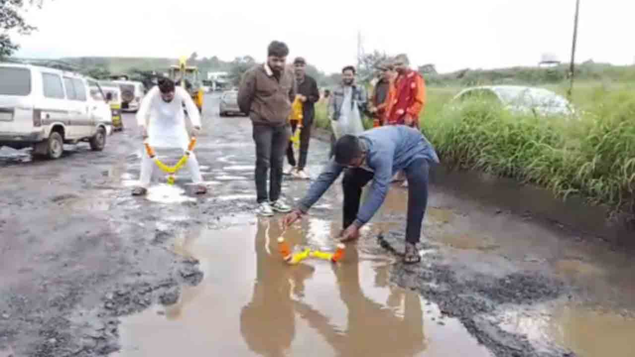 Protesters Garland Potholes | ప్రమాదంలో ఇద్దరు యువకులు మృతి.. గుంతలకు దండలు వేసి నిరసన